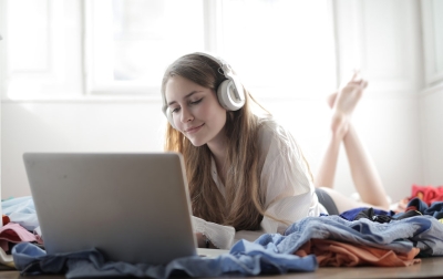 Kanopy resource image showing a young woman with headphones on smiling as she types on a laptop