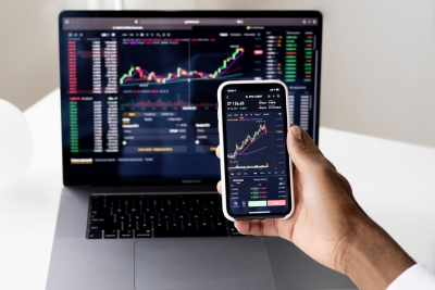 ValueLine resource image showing a person holding a smartphone in front of an open laptop, both displaying stock market charts