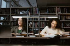 Academic Search Premier resource photo showing two women studying at a table in the library