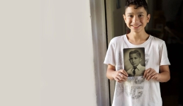 Family Search resource image showing a boy smiling at the camera and holding a black and white photo of an ancestor