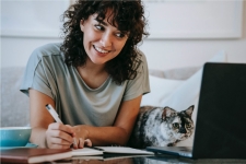 Gale Courses resource image showing a young woman with her cat writing on a piece of paper and smiling at her laptop screen