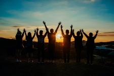 Humanities International Complete resource image showing the silhouette of a group of people with their hands extended in the air looking towards a sunset 