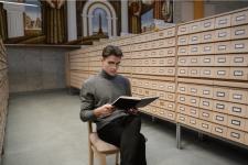 WorldCat.org resource image showing a young man sitting next to catalog cabinets reading a book