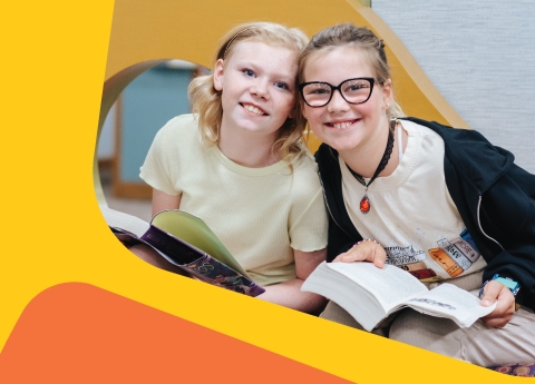 Two tweens reading a book together. 